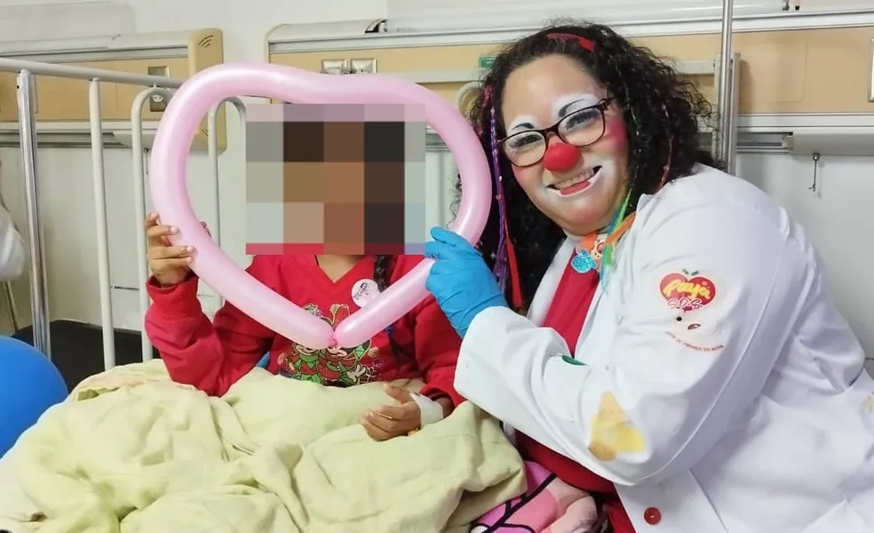 Payasa de hospital junto a una niña con un corazón de globos