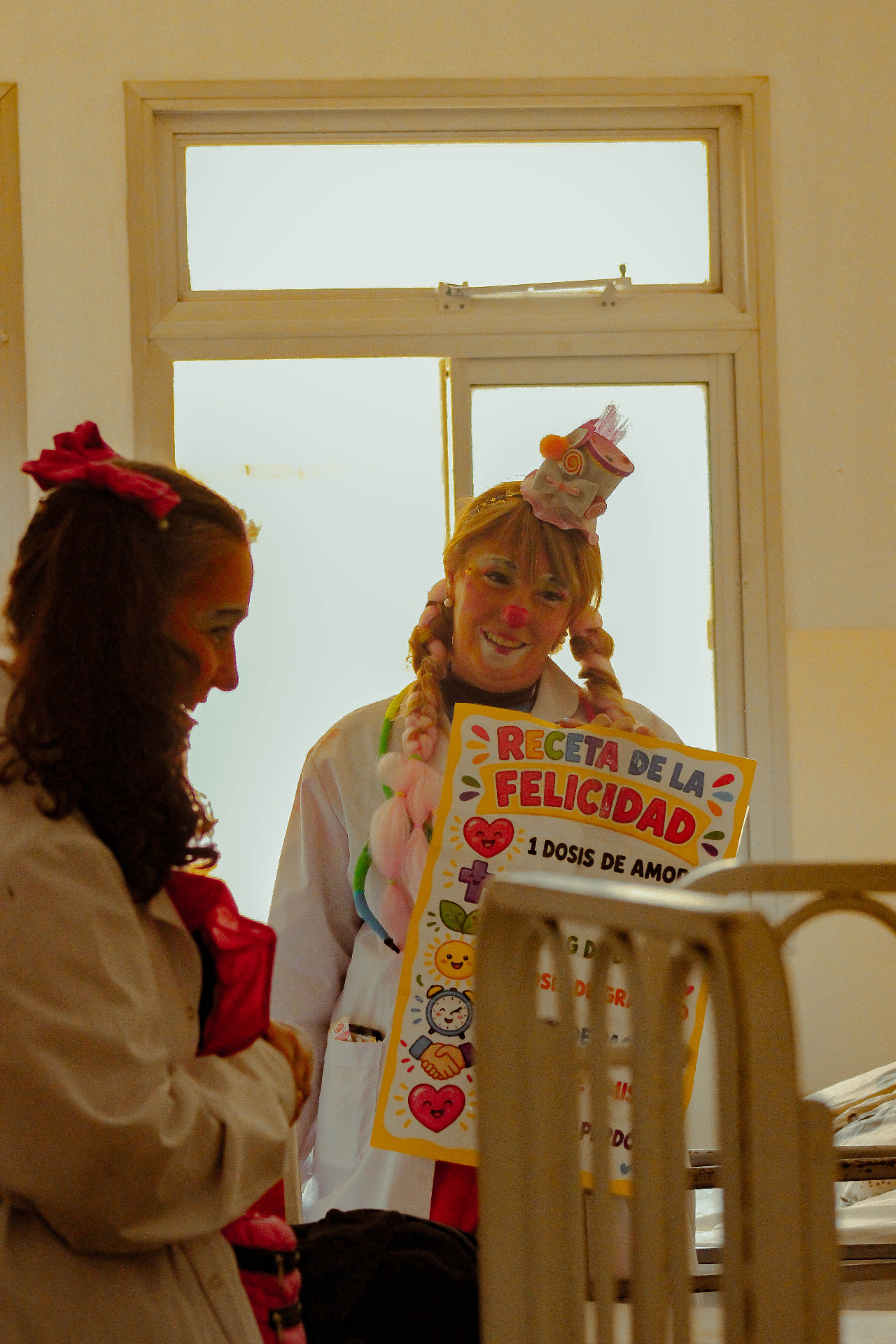 Payasa de PayaSOS 33.3 con el cartel Receta de la Felicidad junto a una niña